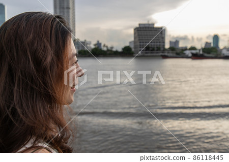 Side view of young woman standing by river and smiles happily. Side view of young woman standing by river and smiles happily. 86118445