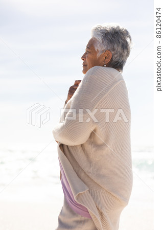 Side view of biracial senior woman with short white hair wearing shrug at beach on sunny day 86120474