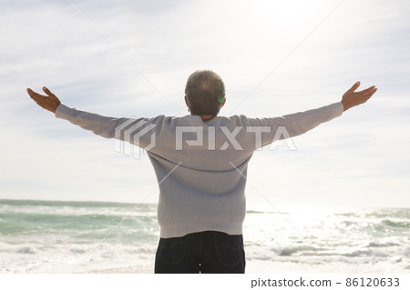 Rear view of biracial senior man with arms outstretched standing at beach during sunny day Rear view of biracial senior man with arms outstretched standing at beach during sunny day 86120633