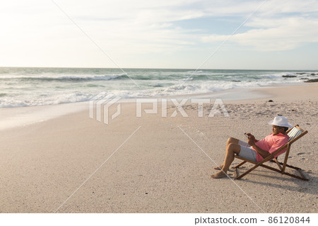 Full length side view of biracial senior man using digital tablet relaxing on folding chair at beach Full length side view of biracial senior man using digital tablet relaxing on folding chair at beach 86120844