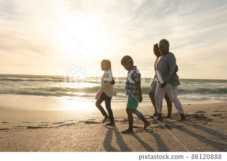 Side view of multiracial grandparents and grandchildren walking on shore at beach during sunset Side view of multiracial grandparents and grandchildren walking on shore at beach during sunset 86120888