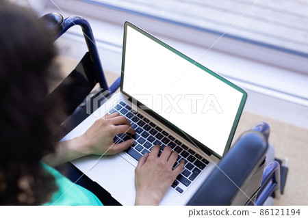 High angle view of biracial disabled woman on wheelchair using laptop with copy space on blank 86121194