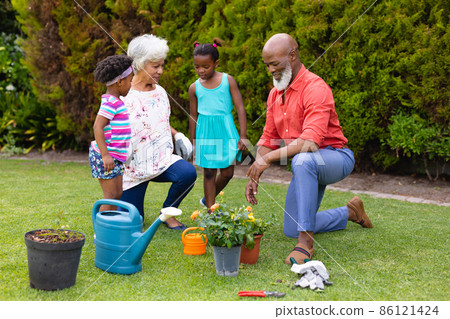 African american grandparents and grandchildren watering plants together in garden 86121424