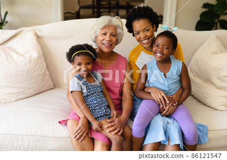 Portrait of smiling african american grandmother, mother and two granddaughters sitting on couch Portrait of smiling african american grandmother, mother and two granddaughters sitting on couch 86121547