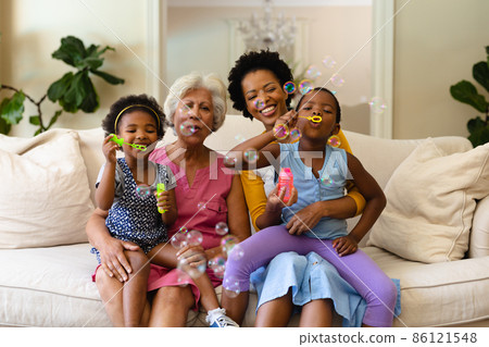 African american grandmother, mother and two granddaughters blowing bubbles sitting on couch African american grandmother, mother and two granddaughters blowing bubbles sitting on couch 86121548