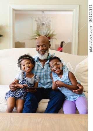 African american grandfather and two granddaughters with digital tablet smiling at home African american grandfather and two granddaughters with digital tablet smiling at home 86121551