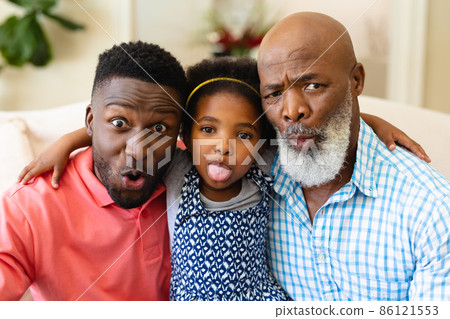 Portrait of african american grandfather, father and granddaughter making silly faces at home Portrait of african american grandfather, father and granddaughter making silly faces at home 86121553