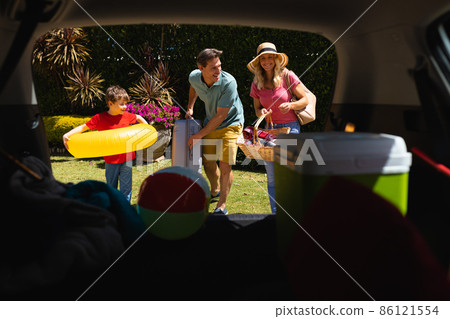 Happy caucasian family putting all their luggage in car Happy caucasian family putting all their luggage in car 86121554