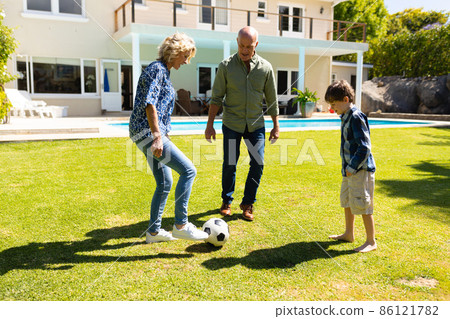 Caucasian grandparents and grandson playing football together in the garden Caucasian grandparents and grandson playing football together in the garden 86121782
