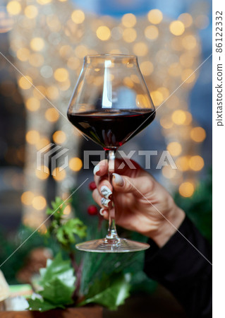 Female hand holding a glass of champagne against the background of a christmas tree, celebrating christmas alone concept, close-up. Female hand holding a glass of champagne against the background of a christmas tree, celebrating christmas alone concept, close-up. 86122332