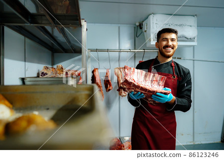 Young butcher holding raw meat steaks in fridge of grocery shop 86123246