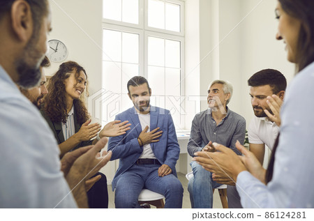 Group of diverse people sit in a circle and applaud their male colleague at a team meeting. Concept of business trainings, group meetings, conferences, seminars, teamwork and brainstorming. 86124281