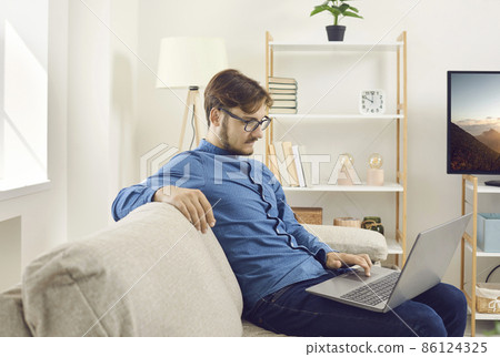 Young caucasian businessman sit on sofa work on computer online, browse wireless internet. Young caucasian businessman sit on sofa work on computer online, browse wireless internet. 86124325