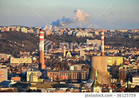 Steaming chimneys with houses in the city. Concept for environment and industry. Background with city landscape at sunset. Brno - Czech Republic - Europe. Steaming chimneys with houses in the city. Concept for environment and industry. Background with city landscape at sunset. Brno - Czech Republic - Europe. 86125759