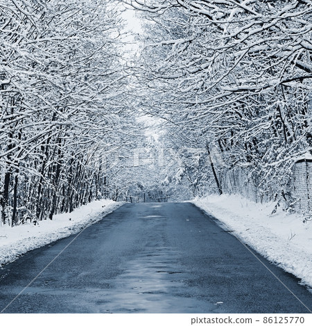 Broken, repaired poor quality asphalt road in winter with snow and icicles. Concept for transport and travel in bad winter weather. 86125770