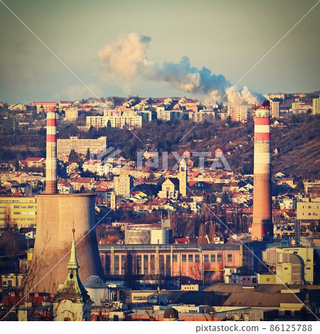 Steaming chimneys with houses in the city. Concept for environment and industry. Background with city landscape at sunset. Brno - Czech Republic - Europe. 86125788