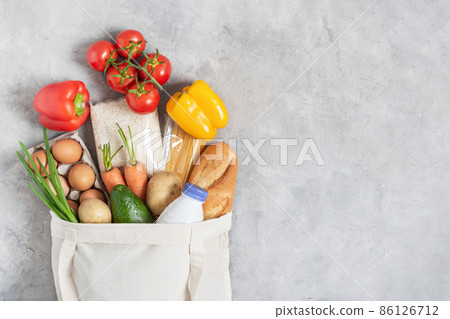 Cotton eco friendly shopping bag full of fresh organic vegetables and grocery products on grey table top view. 86126712