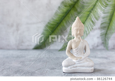 Buddha figure in meditation on grey concrete background with palm leaf. 86126744