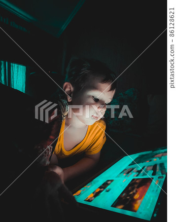 Little boy looking at a tablet in the evening in the dark on the bed Little boy looking at a tablet in the evening in the dark on the bed 86128621
