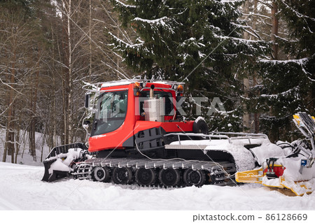 A snowplow on red tracks standing in winter in the forest near the barn A snowplow on red tracks standing in winter in the forest near the barn 86128669