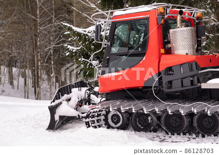 A snowplow on red tracks standing in winter in the forest near the barn A snowplow on red tracks standing in winter in the forest near the barn 86128703