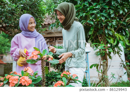 mother and daughter in headscarves chatting while spraying flower plants mother and daughter in headscarves chatting while spraying flower plants 86129943