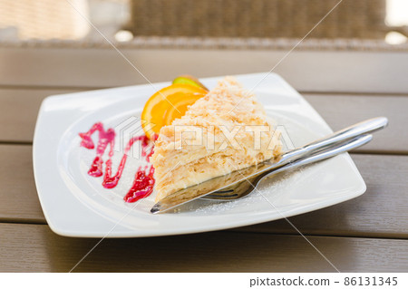 Layered cake with cream Napoleon millefeuille vanilla slice with red jam and fruits on wood background, selective focus, food or menu concept 86131345