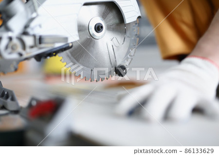 Gloved hands working with a circular saw, close-up Gloved hands working with a circular saw, close-up 86133629