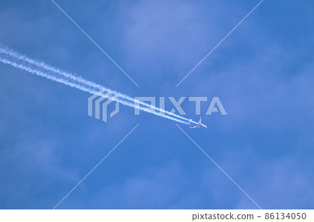 Distant passenger jet plane flying on high altitude through white clouds on blue sky leaving white smoke trace of contrail behind. Air transportation concept 86134050