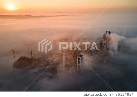 Aerial view of cement factory with high concrete plant structure and tower crane at industrial manufacturing site on foggy evening. Production and global industry concept. 86134054