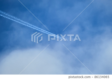 Distant passenger jet plane flying on high altitude through white clouds on blue sky leaving white smoke trace of contrail behind. Air transportation concept Distant passenger jet plane flying on high altitude through white clouds on blue sky leaving white smoke trace of contrail behind. Air transportation concept 86134065