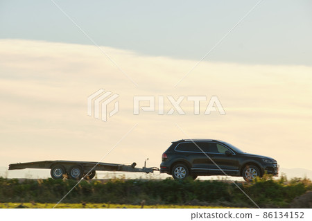 Tow truck vehicle with car transporting carrier trailer driving on highway in evening 86134152