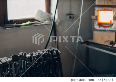 Blacksmith forge oven with hot flame. Smith heating iron piece of steel in fire of red-hot forge with tools Blacksmith forge oven with hot flame. Smith heating iron piece of steel in fire of red-hot forge with tools 86134281