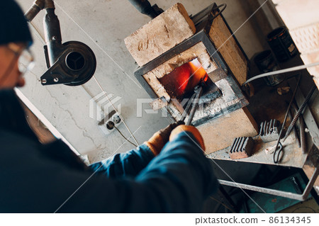 Blacksmith forge oven with hot flame. Smith put in and heating iron piece of steel in fire of red hot forge Blacksmith forge oven with hot flame. Smith put in and heating iron piece of steel in fire of red hot forge 86134345