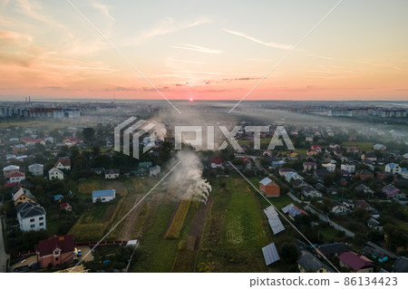 Aerial view of agricultural waste bonfires from dry grass and straw stubble burning with thick smoke polluting air during dry season on farmlands causing global warming and carcinogen fumes Aerial view of agricultural waste bonfires from dry grass and straw stubble burning with thick smoke polluting air during dry season on farmlands causing global warming and carcinogen fumes 86134423