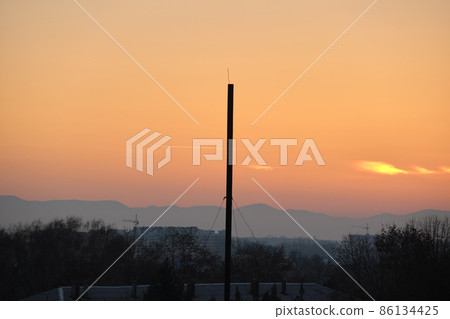 Beautiful evening panoramic landscape with bright setting sun over distant mountain peaks at sunset Beautiful evening panoramic landscape with bright setting sun over distant mountain peaks at sunset 86134425