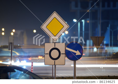 Roundabout road signs with blurred cars on city street traffic at night. Urban transportation concept Roundabout road signs with blurred cars on city street traffic at night. Urban transportation concept 86134625