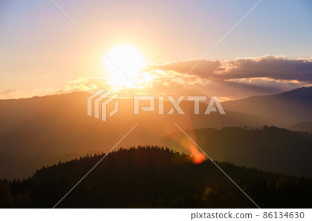 Beautiful evening panoramic landscape with bright setting sun over distant mountain peaks at sunset Beautiful evening panoramic landscape with bright setting sun over distant mountain peaks at sunset 86134630