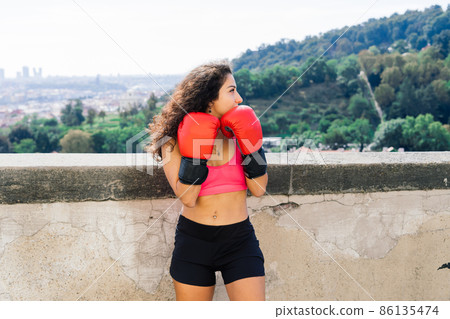 A woman boxer training outdoor - city and nature in background A woman boxer training outdoor - city and nature in background 86135474