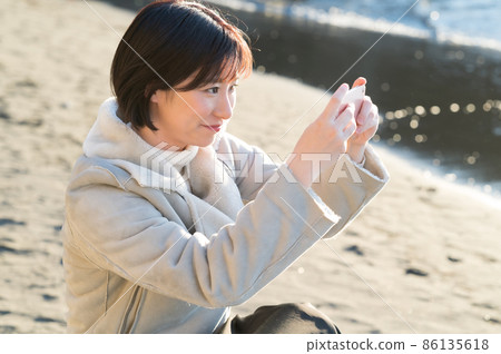 A woman operating a smartphone in the winter sea where the setting sun pours 86135618
