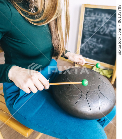 Close-up of a teacher on playing the glucophone. Playing on steel tongue drum. The concept of providing services for meditation, relaxation or music education. Cabinet with a board for inscriptions. Close-up of a teacher on playing the glucophone. Playing on steel tongue drum. The concept of providing services for meditation, relaxation or music education. Cabinet with a board for inscriptions. 86135788