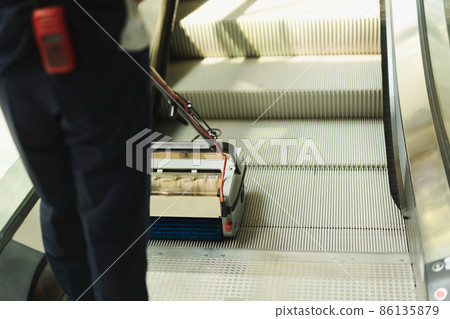 Male cleaner cleaning escalator with mechine in modern building. 86135879