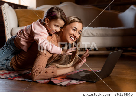 Smiling mom and girl using laptop waving hand Smiling mom and girl using laptop waving hand 86136940
