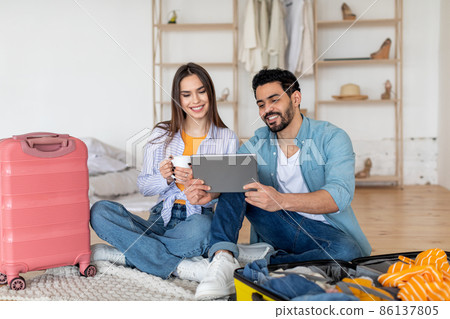 Happy tourists couple using digital tablet and booking travel tickets, choosing destination for next vacation online 86137805