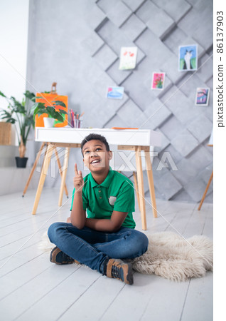 Boy sitting on floor looking pointing finger up Boy sitting on floor looking pointing finger up 86137903