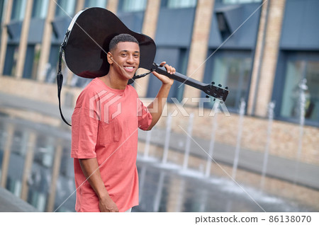 Man looking at camera holding guitar on his shoulder Man looking at camera holding guitar on his shoulder 86138070