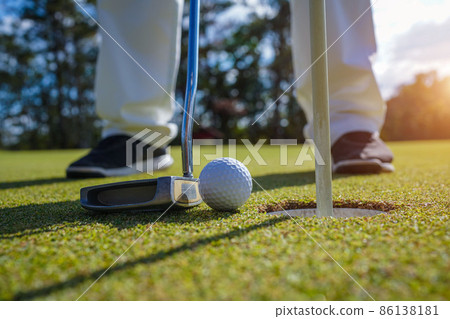 Golfer putting ball on the green golf, lens flare on sun set evening time. Golfer action to win after long putting golf ball in to the hole Golfer putting ball on the green golf, lens flare on sun set evening time. Golfer action to win after long putting golf ball in to the hole 86138181