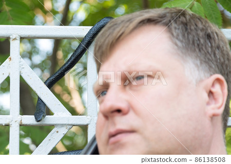 A black venomous snake on a metal fence crept up to a man talking on the phone A black venomous snake on a metal fence crept up to a man talking on the phone 86138508