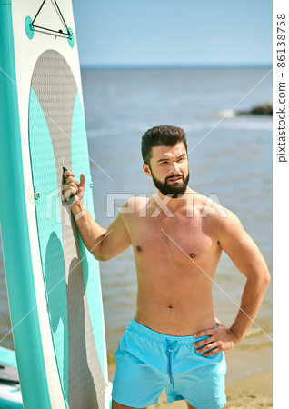A well-built young man with a surfing board on a beach A well-built young man with a surfing board on a beach 86138758