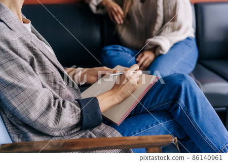 Close-up of a psychologist's hands writing down notes about a patient in a notebook. 86140961